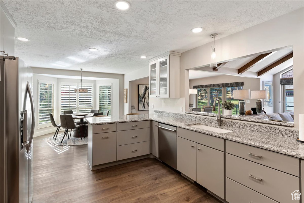Kitchen with stainless steel appliances, a peninsula, a textured ceiling, dark wood finished floors, and glass insert cabinets