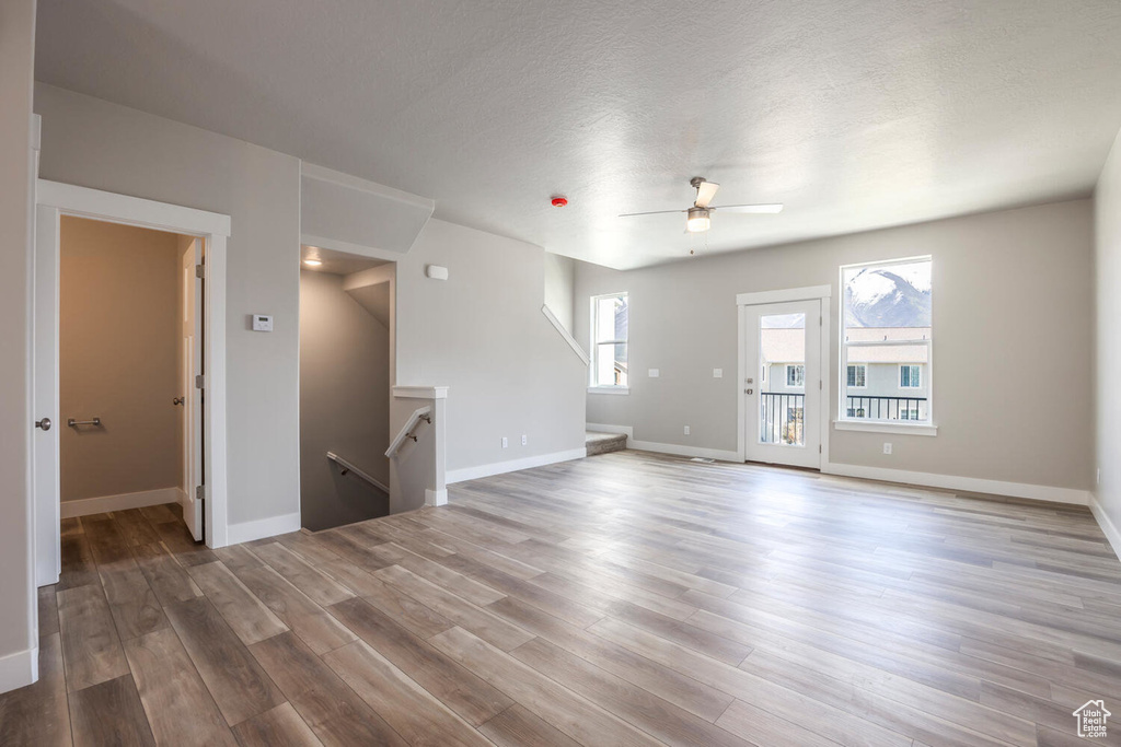 Unfurnished living room featuring a ceiling fan, wood finished floors, and a textured ceiling
