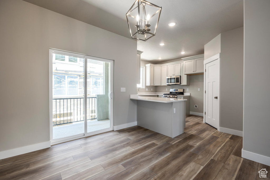 Kitchen with appliances with stainless steel finishes, a peninsula, a chandelier, light countertops, and wood finished floors