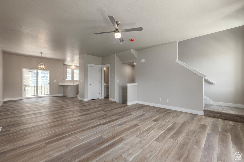 Unfurnished living room with light wood finished floors, ceiling fan, a chandelier, and stairway