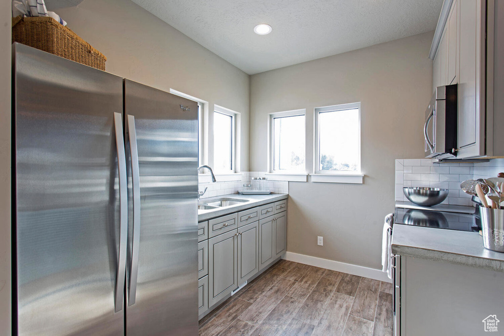Kitchen with appliances with stainless steel finishes, gray cabinetry, tasteful backsplash, light countertops, and light wood finished floors