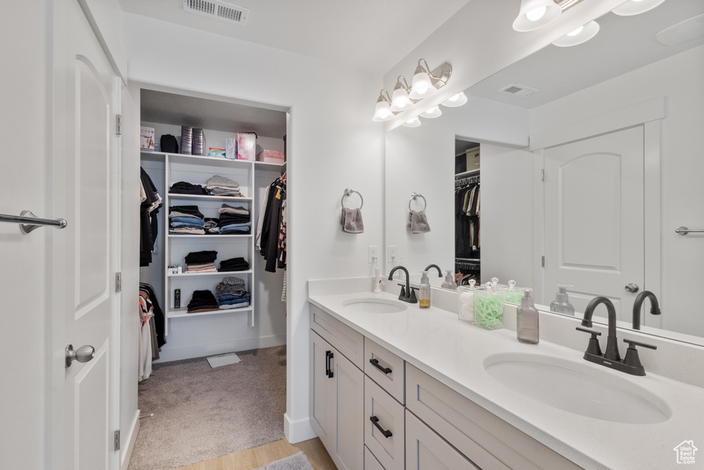 Bathroom with double vanity, a walk in closet, and wood finished floors