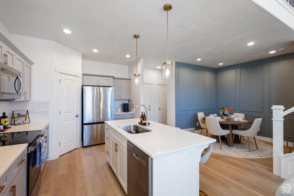 Kitchen featuring appliances with stainless steel finishes, light wood-style flooring, a decorative wall, light countertops, and tasteful backsplash