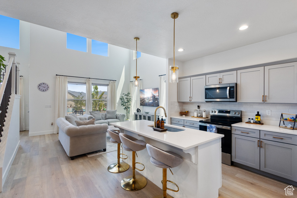 Kitchen with stainless steel appliances, gray cabinetry, decorative backsplash, light countertops, and light wood-style flooring