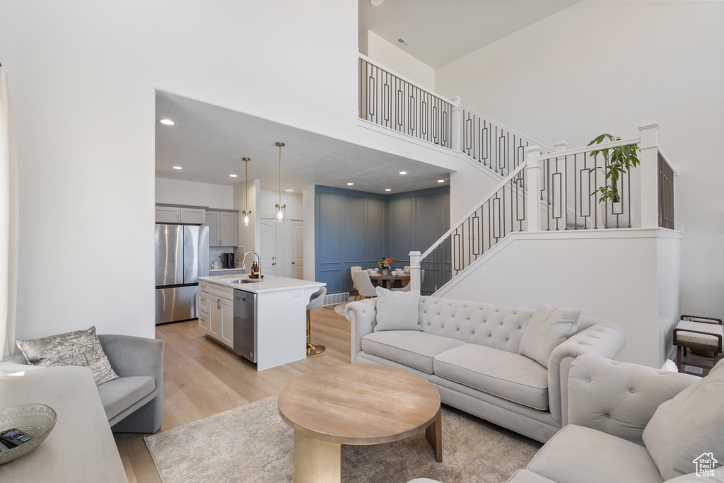 Living area featuring a high ceiling, light wood-style flooring, stairs, and recessed lighting