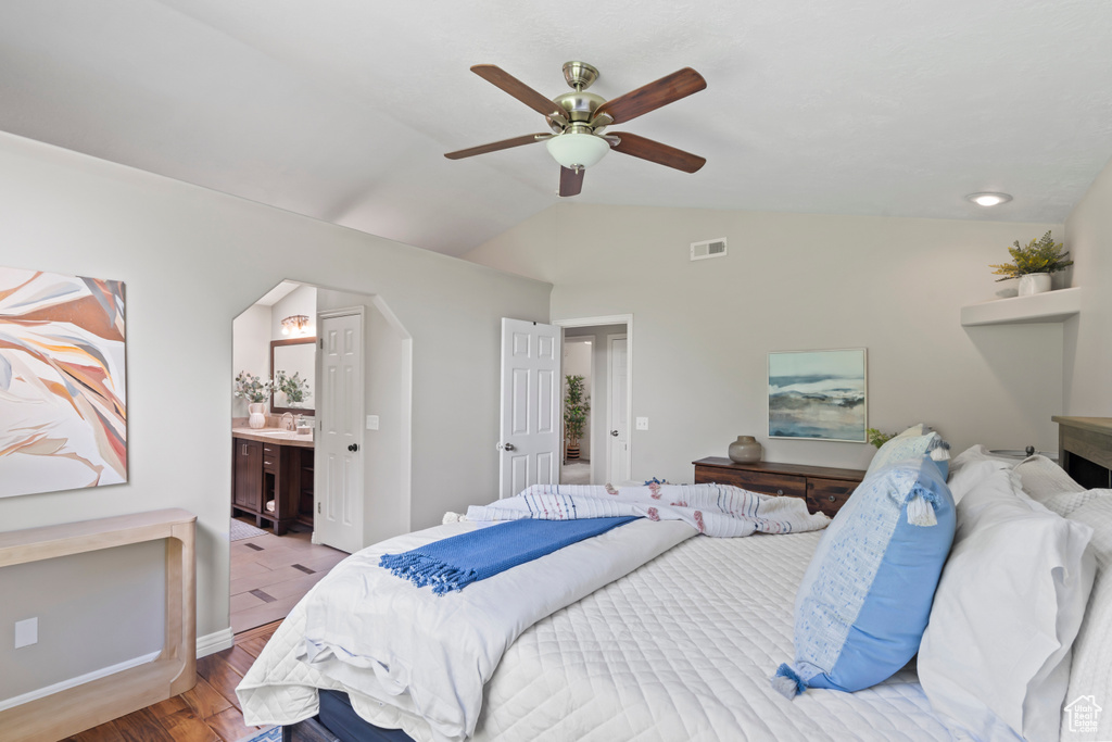 Bedroom with wood finished floors, vaulted ceiling, connected bathroom, a ceiling fan, and arched walkways