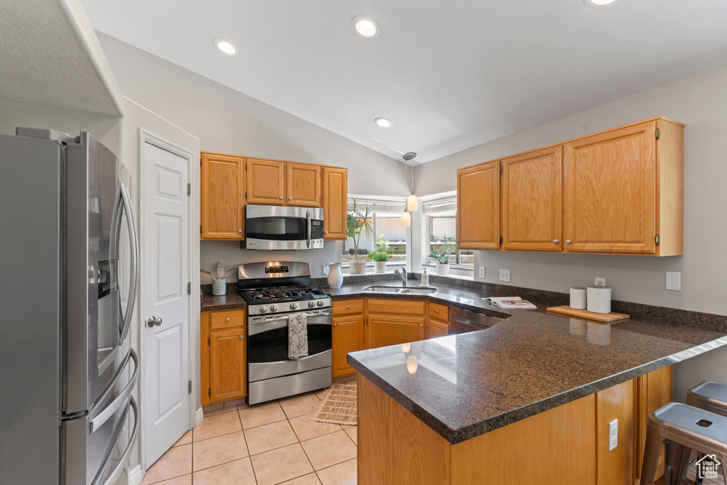 Kitchen featuring appliances with stainless steel finishes, a peninsula, lofted ceiling, light tile patterned flooring, and recessed lighting