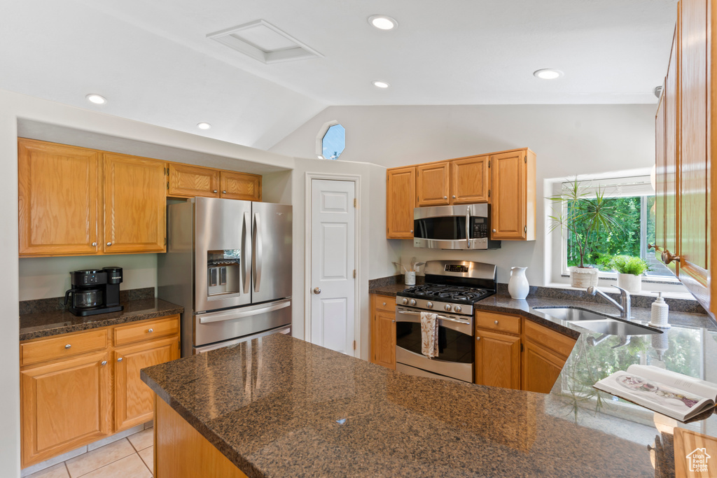 Kitchen featuring stainless steel appliances, lofted ceiling, dark stone counters, a peninsula, and light tile patterned flooring