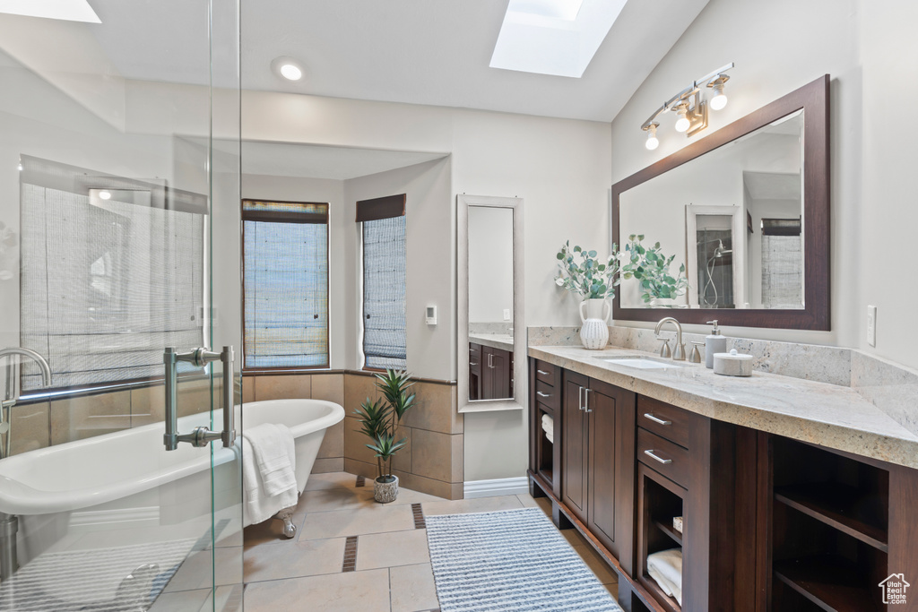 Full bath with a skylight, vanity, tile patterned floors, a freestanding tub, and tile walls