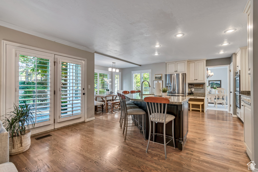 Kitchen with appliances with stainless steel finishes, a center island with sink, a kitchen breakfast bar, recessed lighting, and wood finished floors