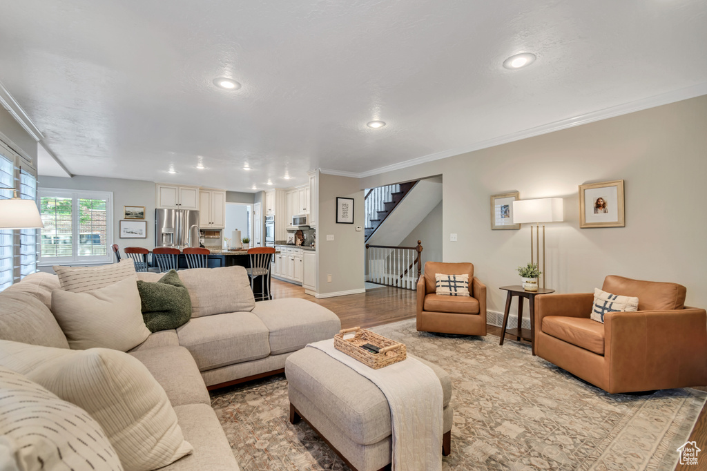 Living area featuring light wood finished floors, stairs, ornamental molding, and recessed lighting