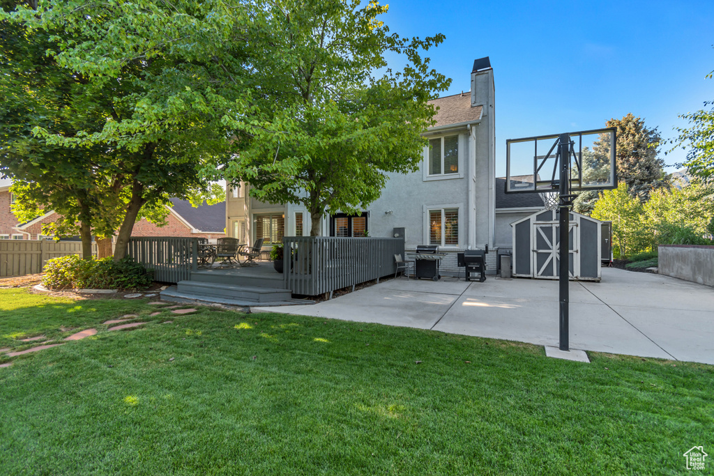 Rear view of house featuring a shed, stucco siding, a deck, a patio area, and a chimney