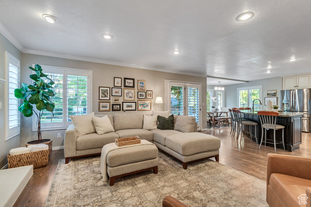 Living area with light wood-type flooring, healthy amount of natural light, ornamental molding, and recessed lighting