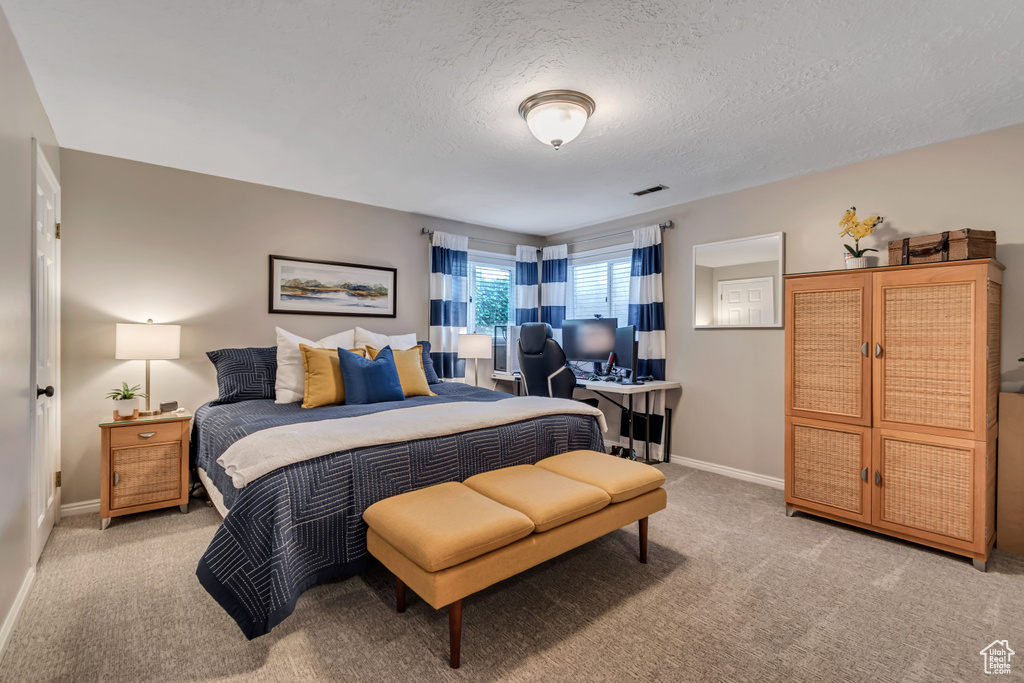 Bedroom with light carpet, a desk, and a textured ceiling