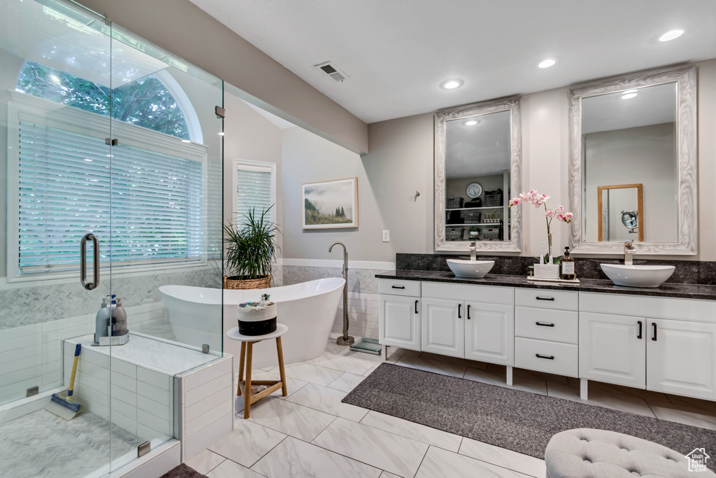 Full bathroom featuring double vanity, a freestanding bath, a stall shower, tile walls, and a wainscoted wall