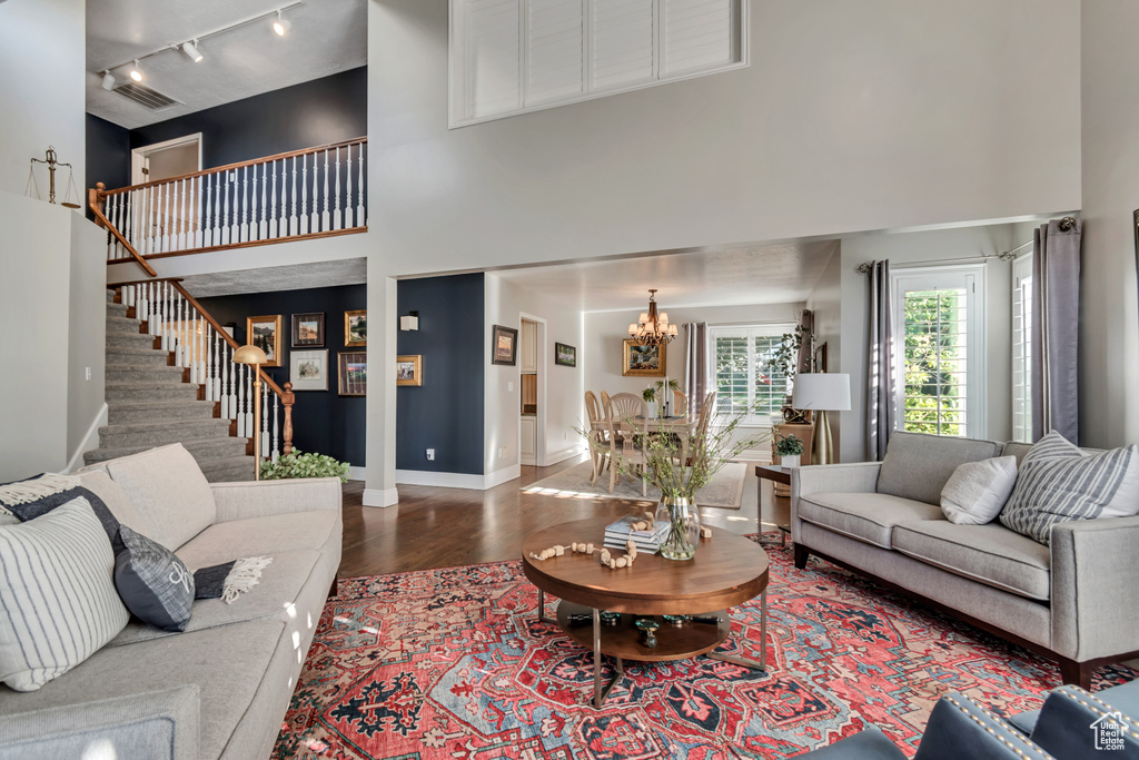 Living area with a high ceiling, rail lighting, a chandelier, stairs, and wood finished floors