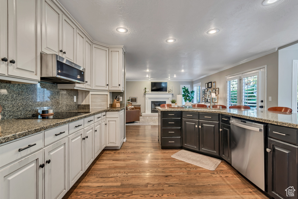 Kitchen with stainless steel appliances, open floor plan, recessed lighting, light wood-style flooring, and ornamental molding