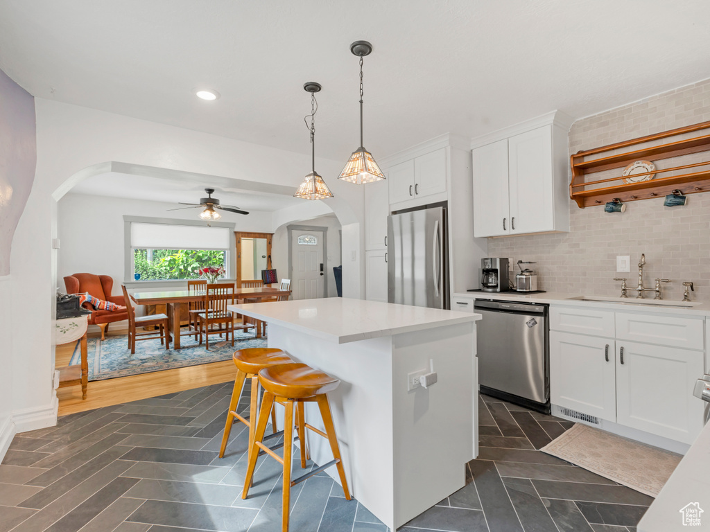 Kitchen with appliances with stainless steel finishes, arched walkways, ceiling fan, white cabinets, and a center island