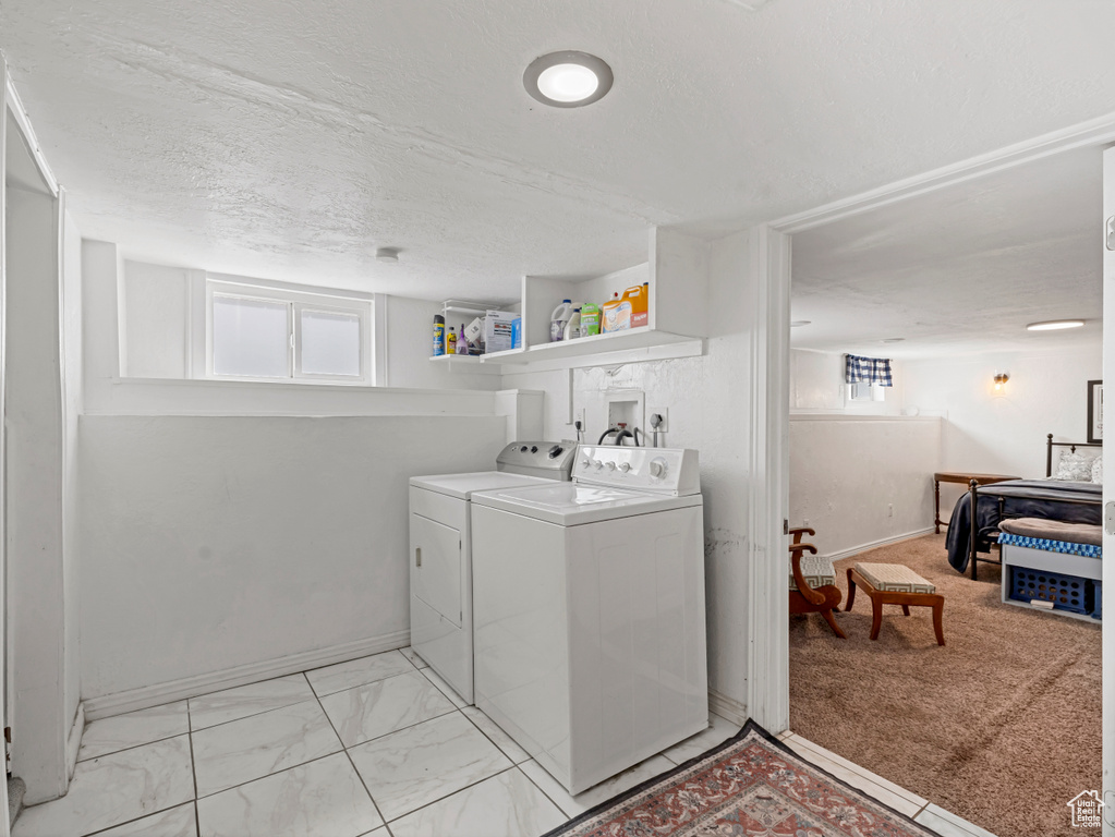 Laundry area with washing machine and clothes dryer, plenty of natural light, a textured ceiling, and light marble finish flooring