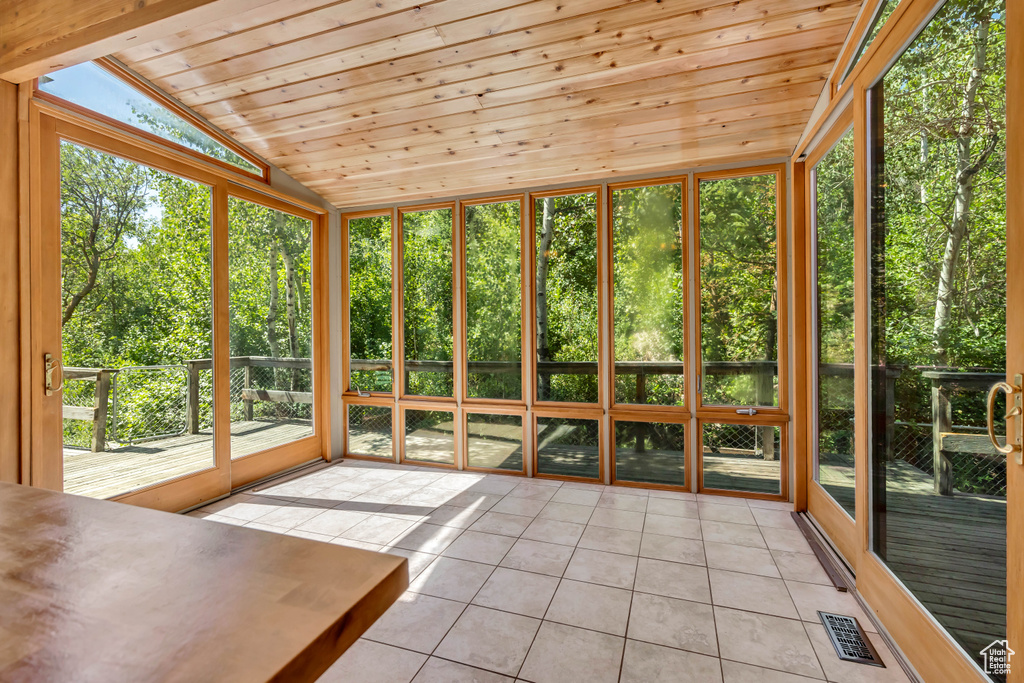 Unfurnished sunroom with tile patterned flooring, lofted ceiling, wooden ceiling, and a deck