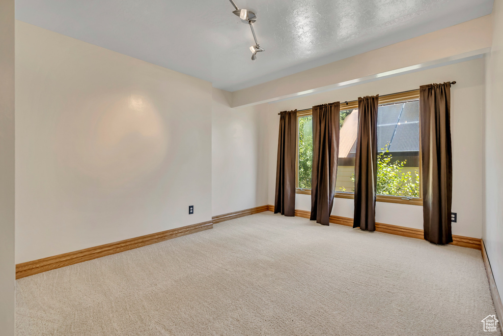 Empty room featuring light colored carpet and rail lighting