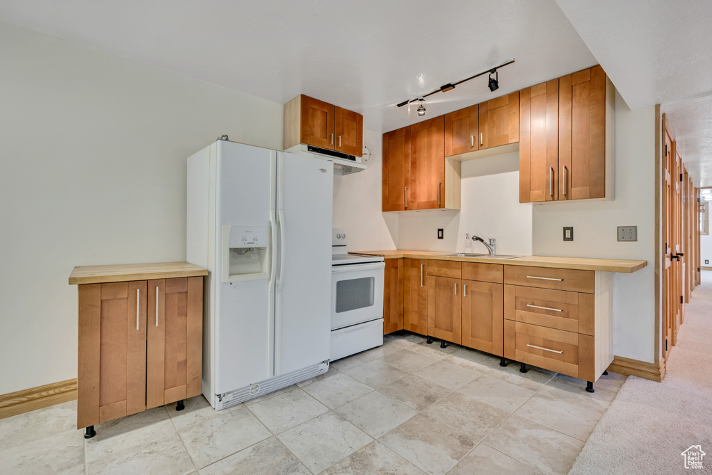 Kitchen featuring white appliances, under cabinet range hood, track lighting, light countertops, and brown cabinetry