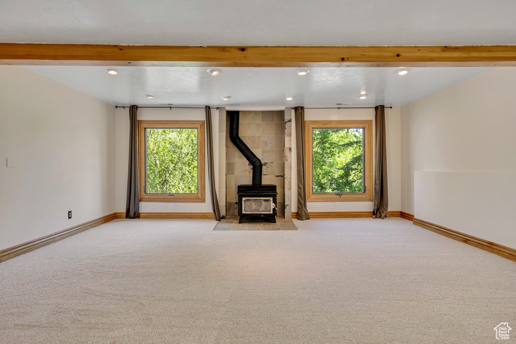 Unfurnished living room with a wood stove, recessed lighting, healthy amount of natural light, carpet floors, and beamed ceiling