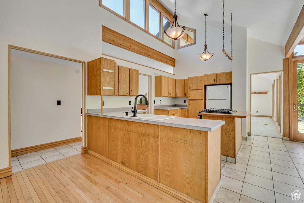Kitchen with high vaulted ceiling, freestanding refrigerator, a peninsula, light countertops, and pendant lighting