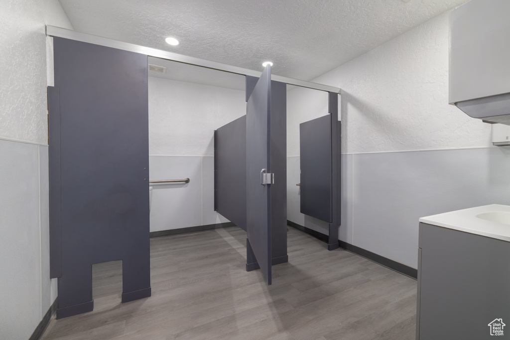 Bathroom with a textured ceiling, wood finished floors, vanity, and a textured wall