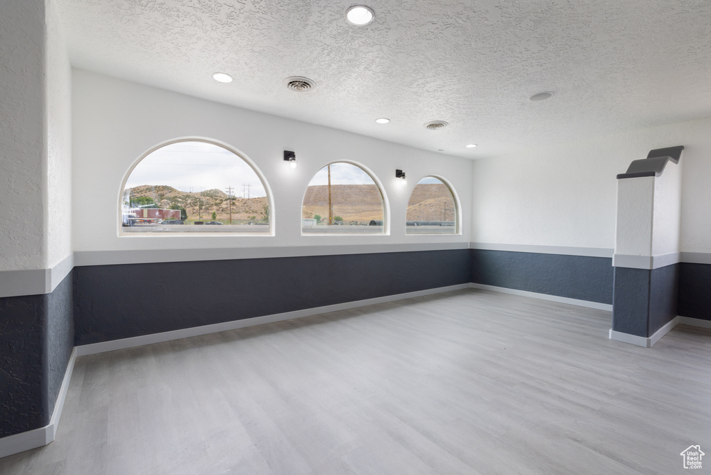 Empty room featuring healthy amount of natural light, a textured ceiling, wood finished floors, and recessed lighting