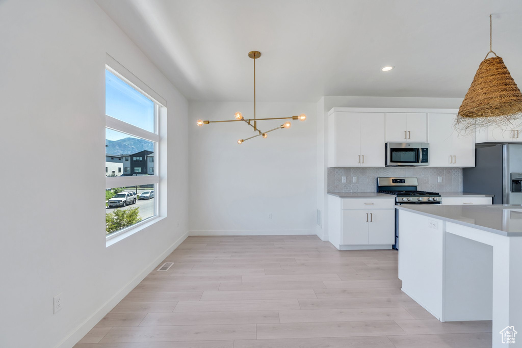 Kitchen with stainless steel appliances, a chandelier, decorative backsplash, decorative light fixtures, and light countertops