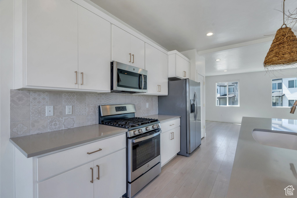 Kitchen featuring appliances with stainless steel finishes, white cabinetry, backsplash, light wood-type flooring, and recessed lighting