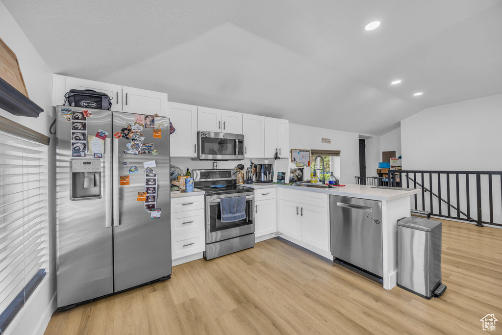 Kitchen with appliances with stainless steel finishes, vaulted ceiling, a peninsula, white cabinets, and light wood finished floors