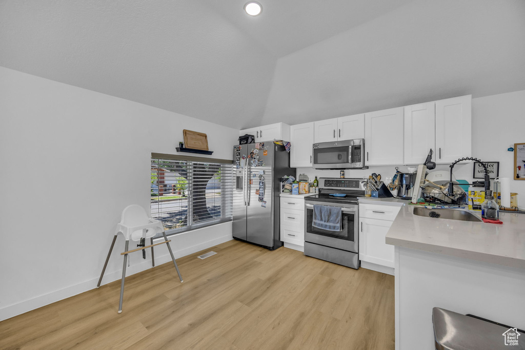 Kitchen featuring appliances with stainless steel finishes, white cabinetry, light wood-style floors, and high vaulted ceiling