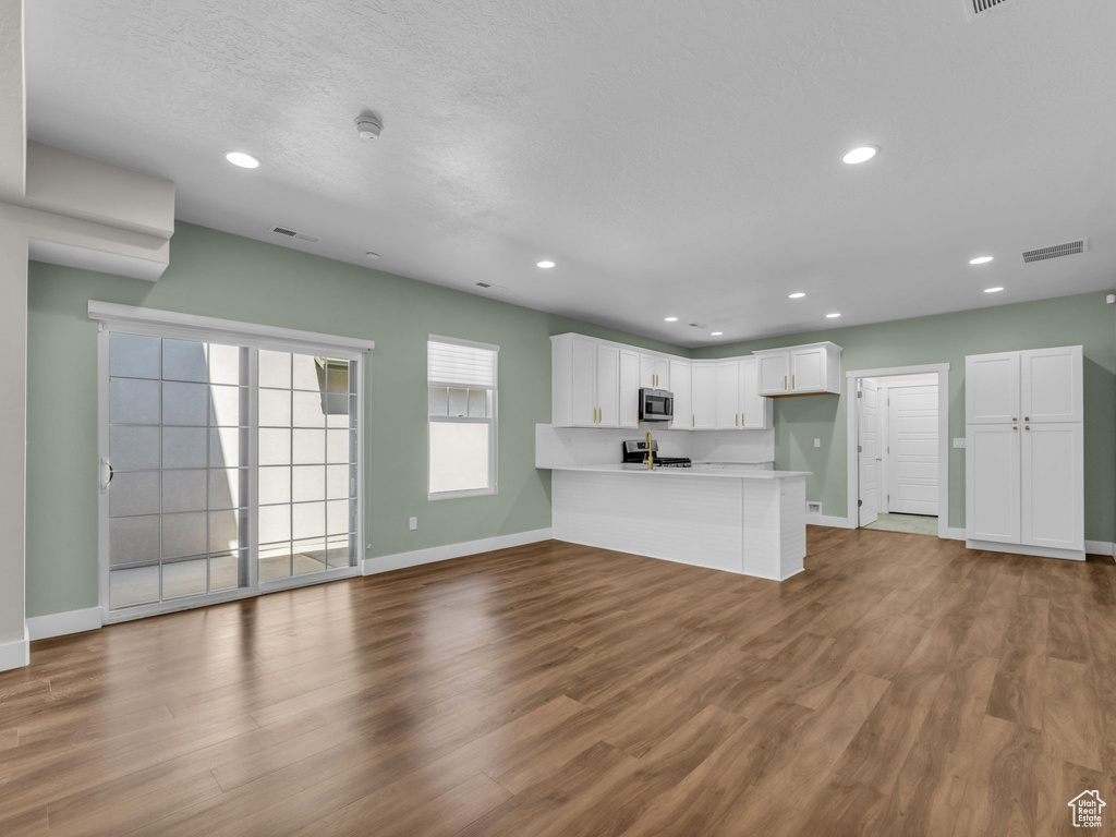 Kitchen featuring stainless steel microwave, a peninsula, range, white cabinetry, and recessed lighting