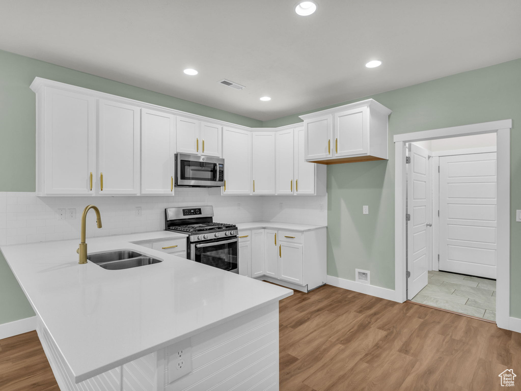 Kitchen featuring appliances with stainless steel finishes, a peninsula, light countertops, white cabinets, and recessed lighting