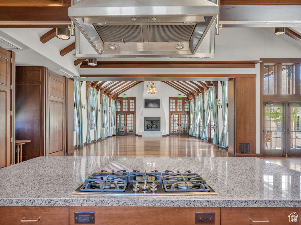Kitchen featuring stainless steel gas cooktop, ventilation hood, open floor plan, brown cabinetry, and beamed ceiling
