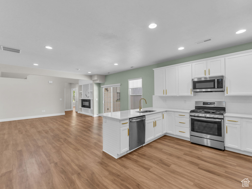 Kitchen featuring appliances with stainless steel finishes, a peninsula, light countertops, white cabinetry, and open floor plan