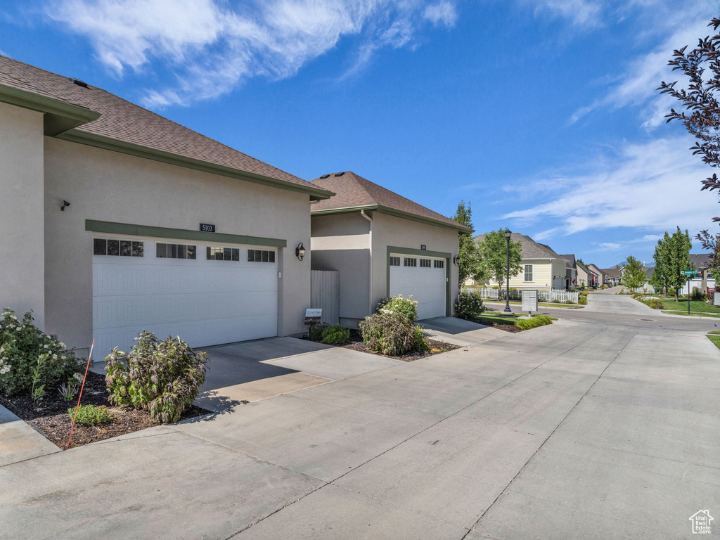 View of home\'s exterior with stucco siding, driveway, an attached garage, a residential view, and a shingled roof