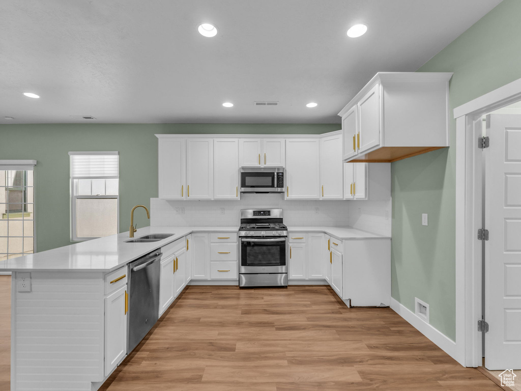 Kitchen with stainless steel appliances, a peninsula, light countertops, white cabinetry, and light wood-style floors
