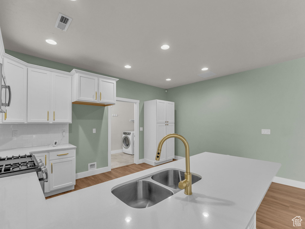 Kitchen featuring washer / dryer, appliances with stainless steel finishes, white cabinets, light wood-type flooring, and backsplash