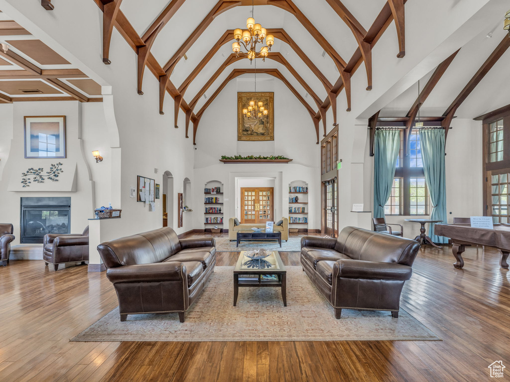 Living area featuring a chandelier, high vaulted ceiling, hardwood / wood-style flooring, a glass covered fireplace, and beam ceiling