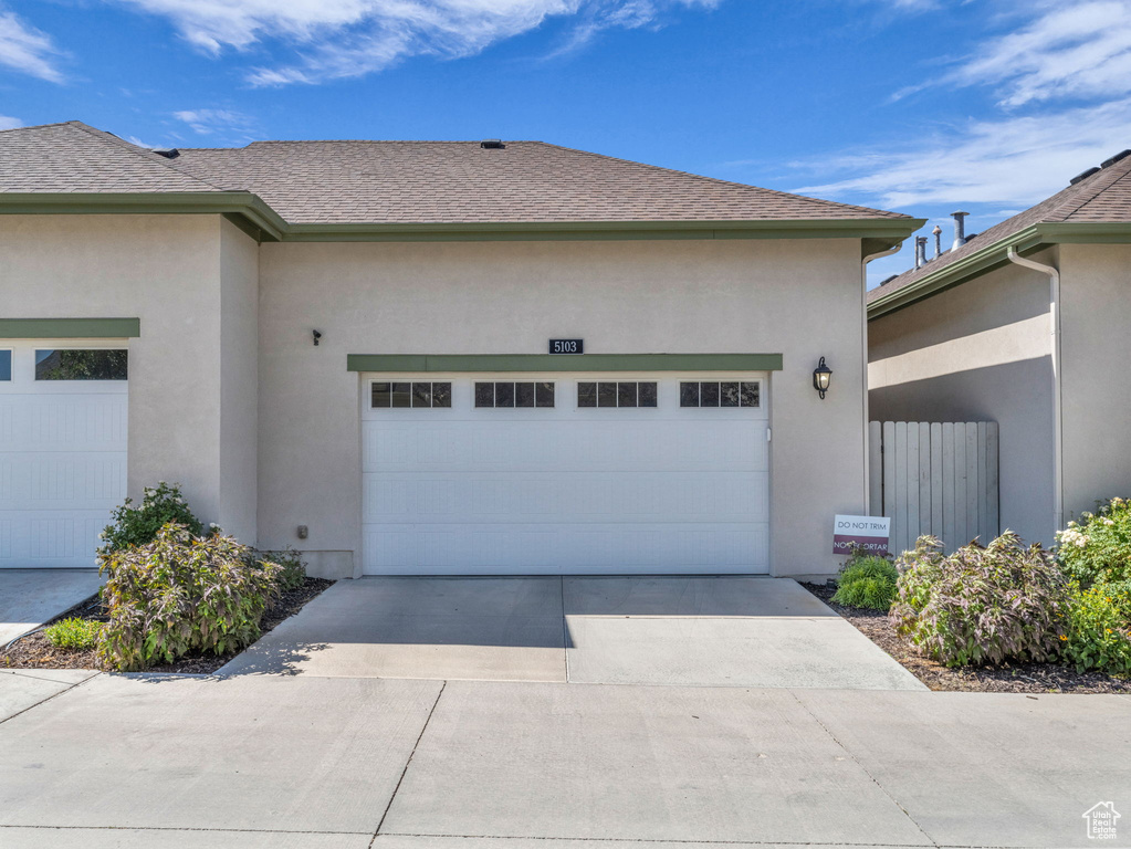 View of home\'s exterior featuring an attached garage, driveway, stucco siding, and roof with shingles