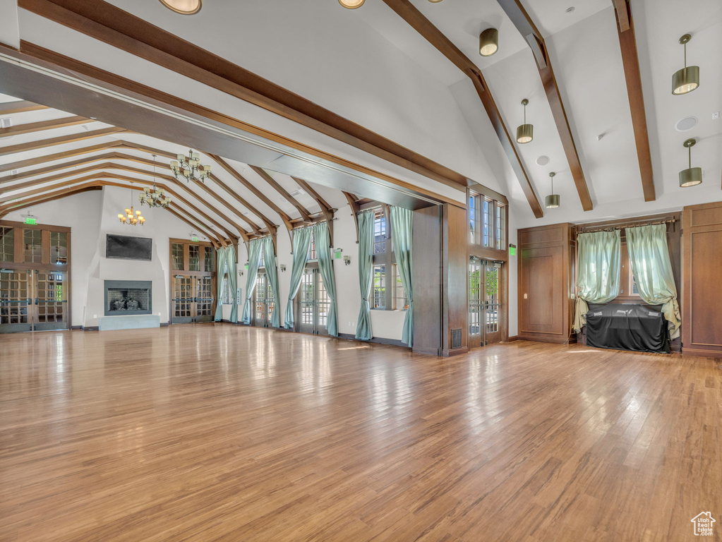 Unfurnished living room with beam ceiling, high vaulted ceiling, a chandelier, a fireplace with raised hearth, and light wood-style floors