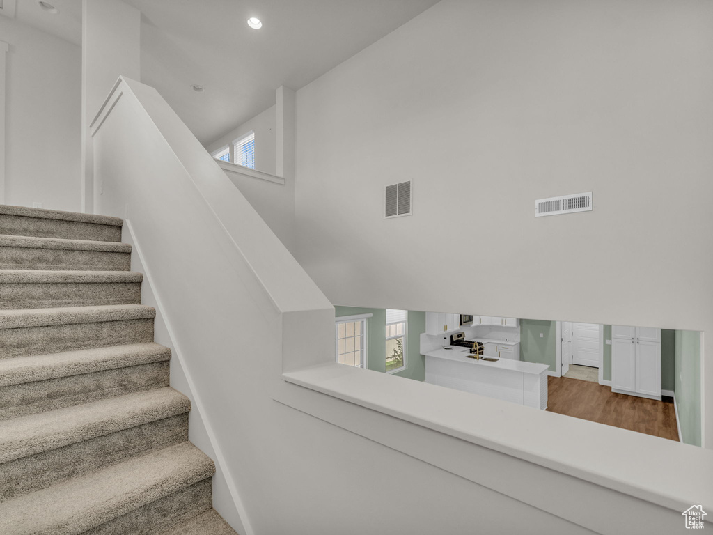 Staircase featuring recessed lighting, wood finished floors, and a towering ceiling