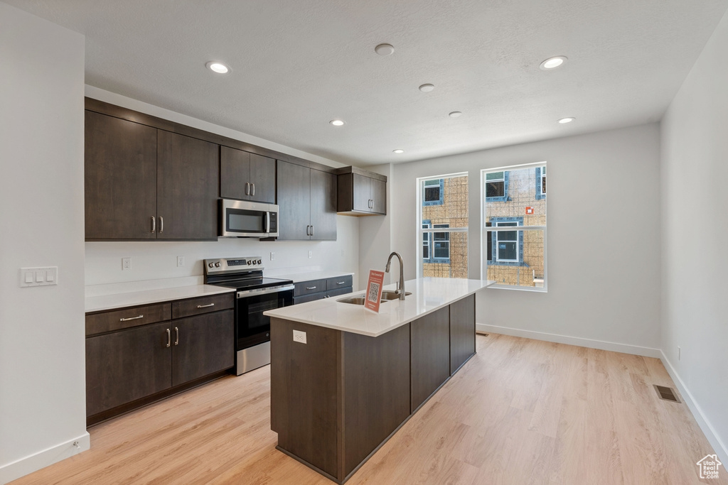 Kitchen with appliances with stainless steel finishes, light wood-type flooring, light countertops, dark brown cabinetry, and recessed lighting