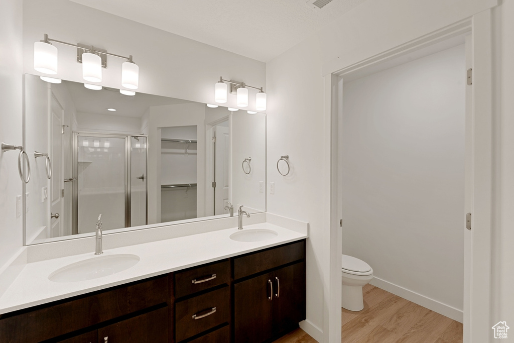 Bathroom featuring a stall shower, wood finished floors, a walk in closet, and double vanity