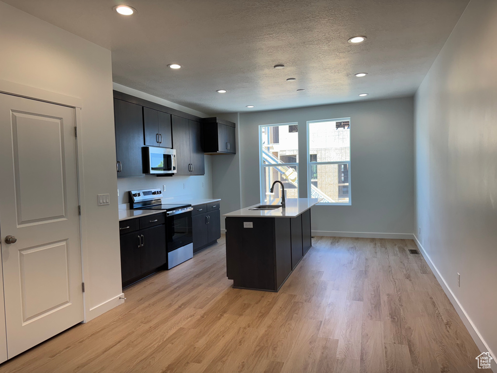 Kitchen featuring appliances with stainless steel finishes, dark cabinets, light wood-style flooring, light countertops, and recessed lighting