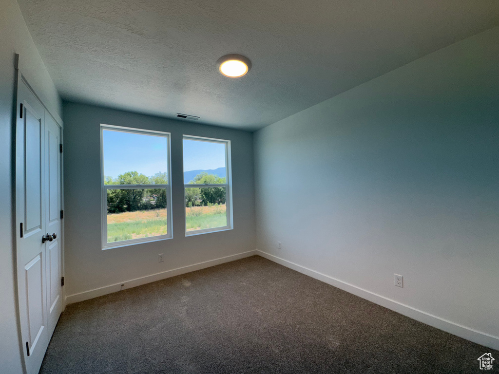 Empty room with dark carpet and a textured ceiling