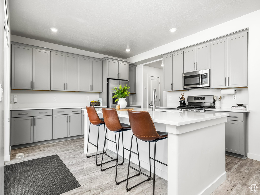 Kitchen with appliances with stainless steel finishes, gray cabinets, light wood-style flooring, a kitchen breakfast bar, and recessed lighting